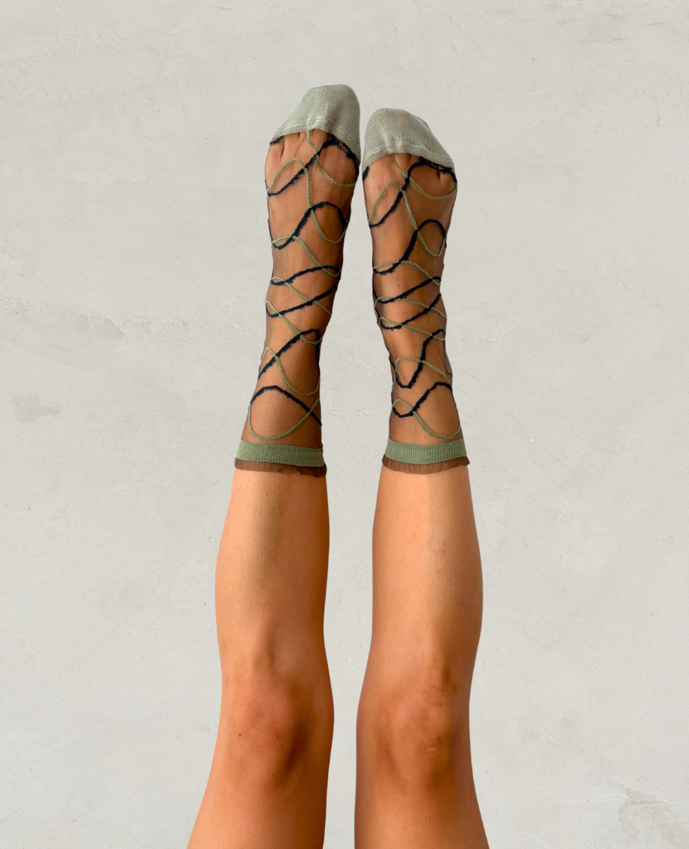 Sheer socks with black wavy pattern worn by a person on a plain background