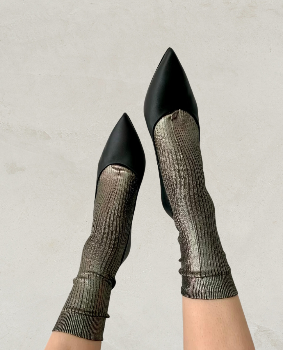 Black pointed-toe shoes with a smooth, matte finish are paired with metallic, ribbed socks that have a shimmering texture and a snug fit.