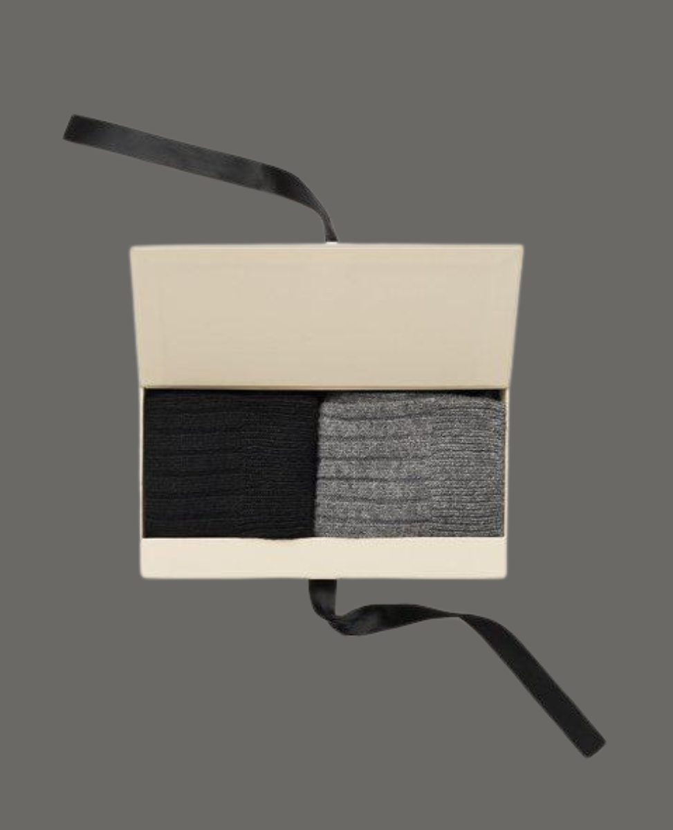 A beige rectangular box with a black ribbon contains two pairs of ribbed socks, one black and one gray, neatly folded side by side.