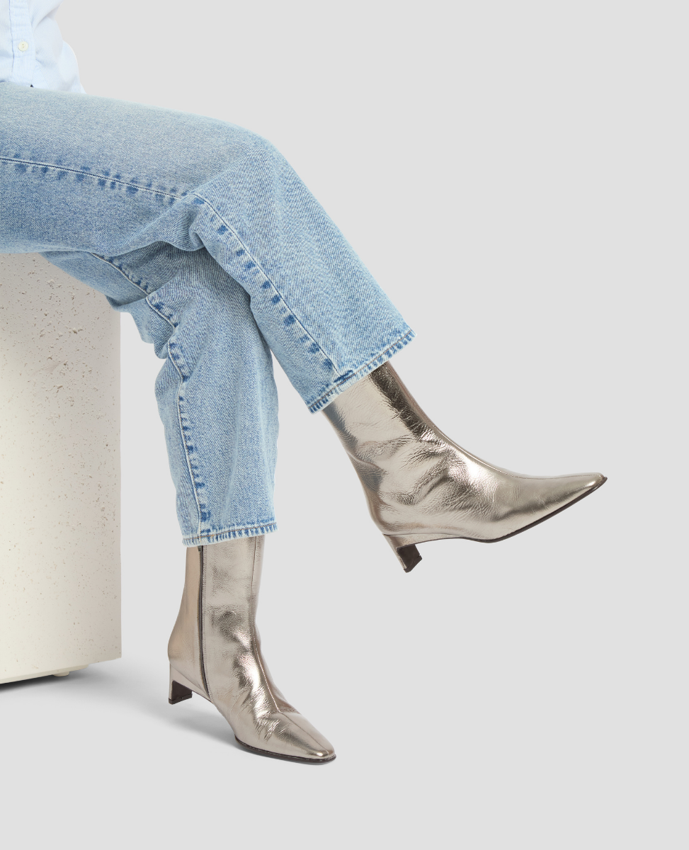 Person wearing metallic knee-high boots and light blue jeans on a white background