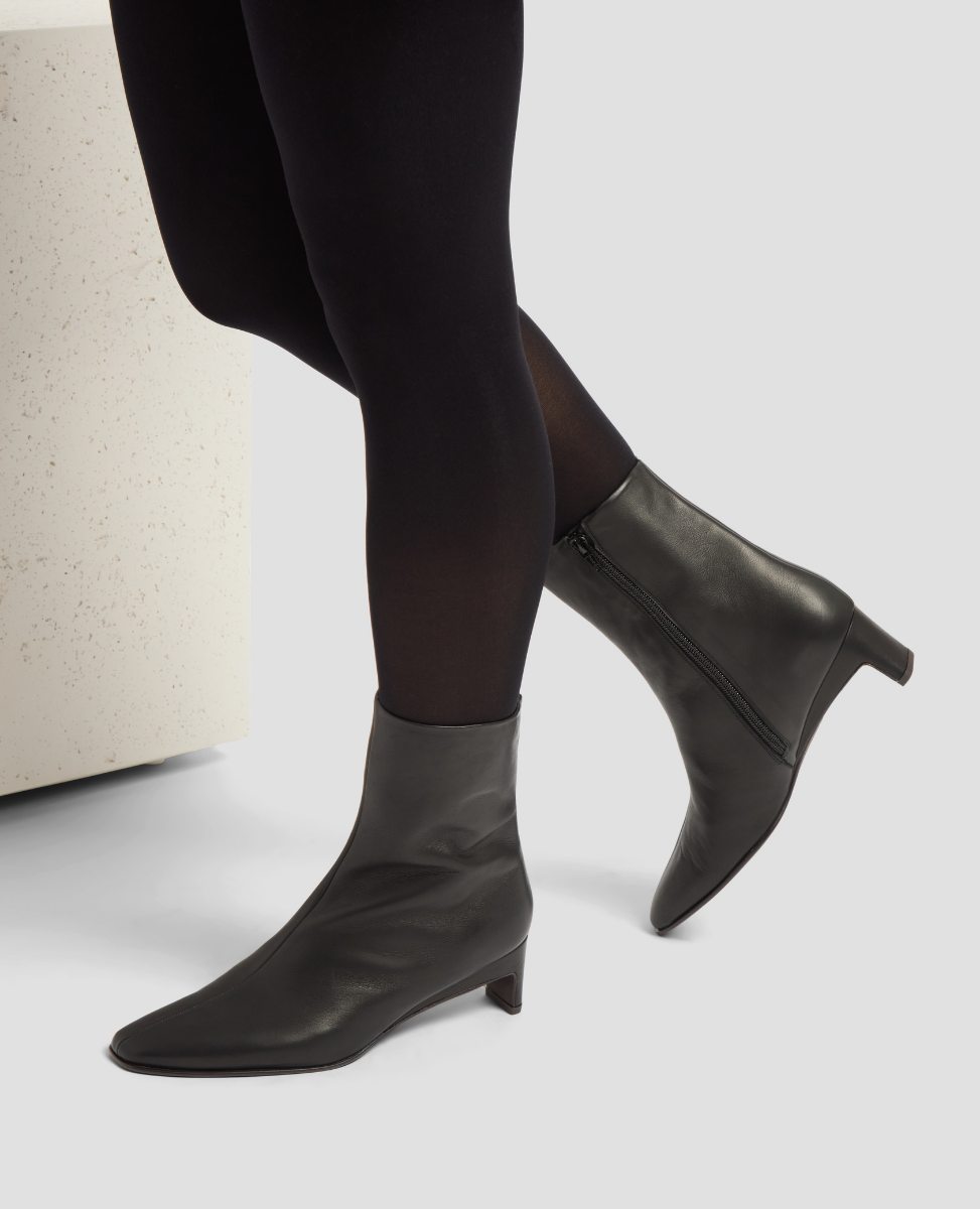 Black ankle boots worn with black tights on a light gray background