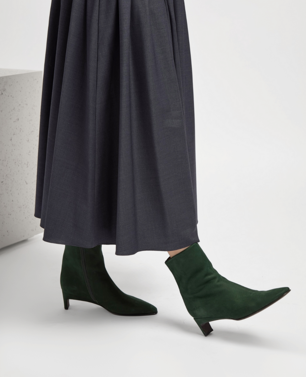 Person wearing green sock boots with a long dark gray skirt on a light background
