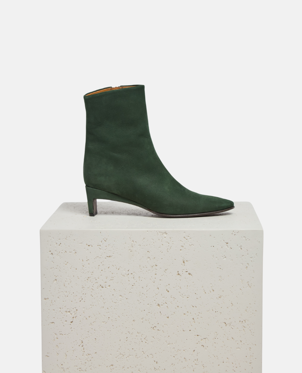 Green ankle boot on a white pedestal with a light gray background
