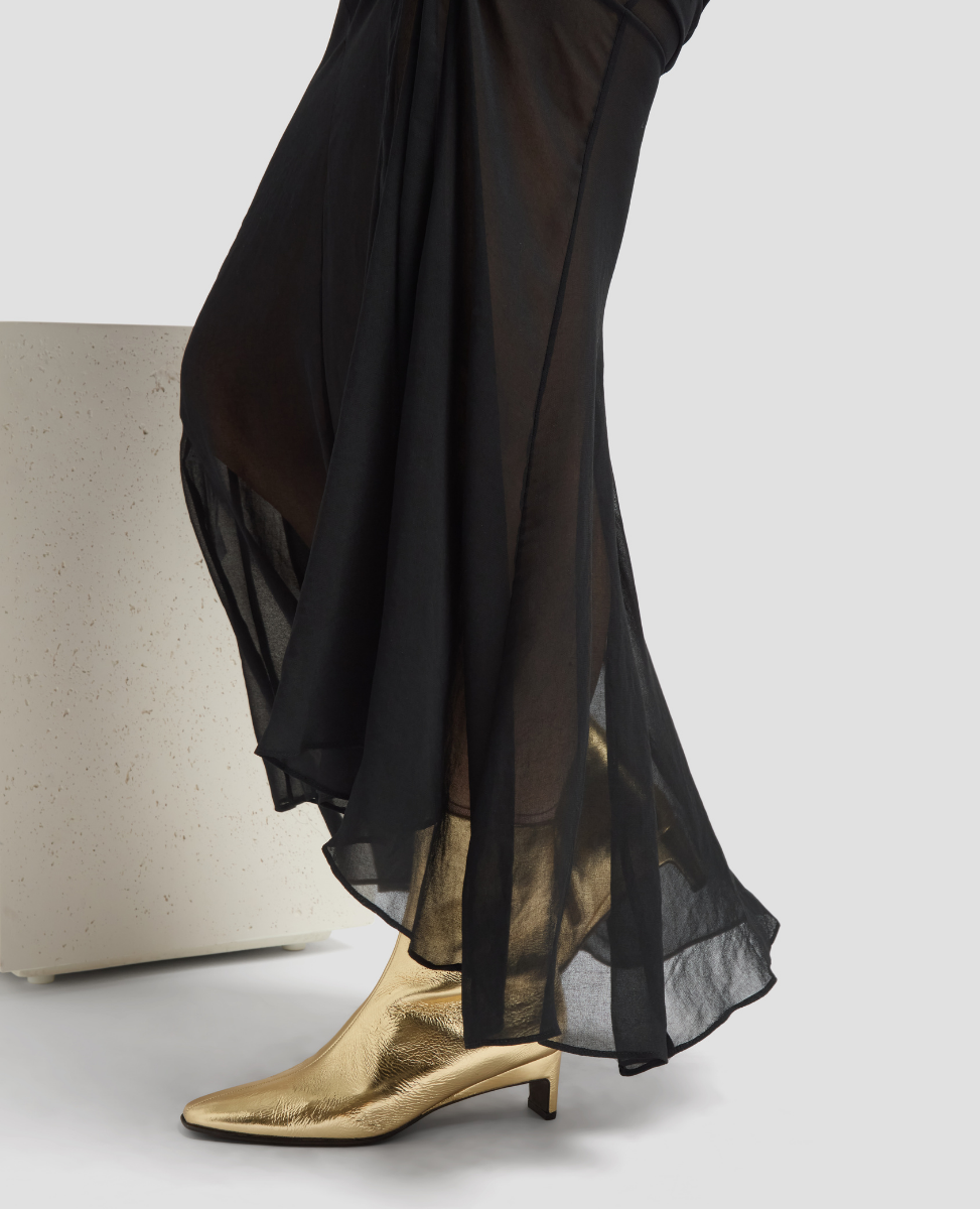 Black sheer skirt with gold high-heeled shoes on a light gray background