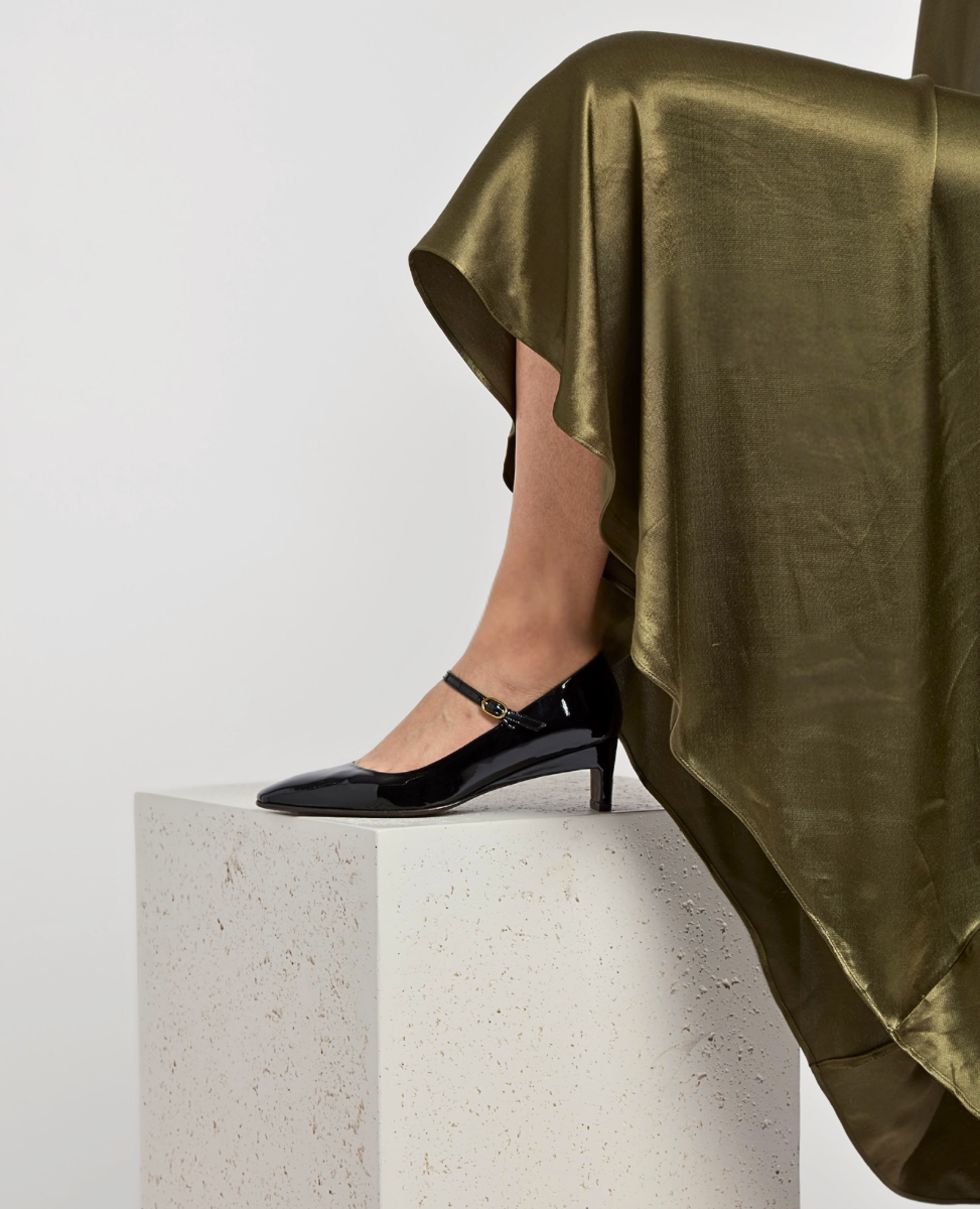 Person wearing black high-heeled shoes with a green satin skirt on a white background