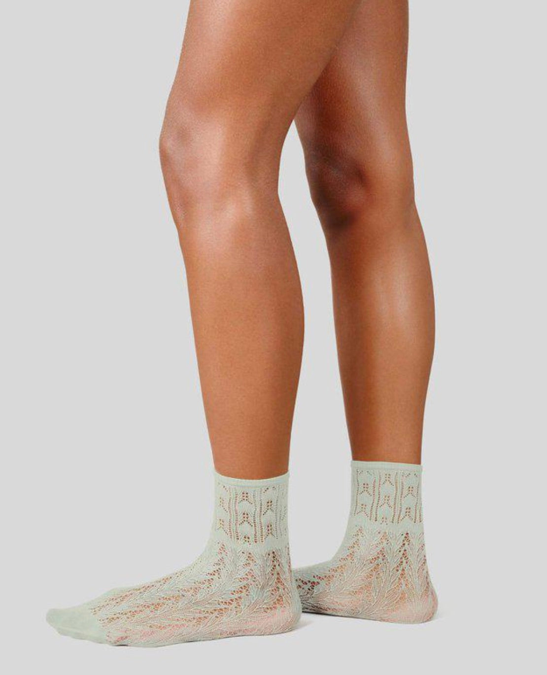 Person wearing light green socks with a subtle pattern on a plain background