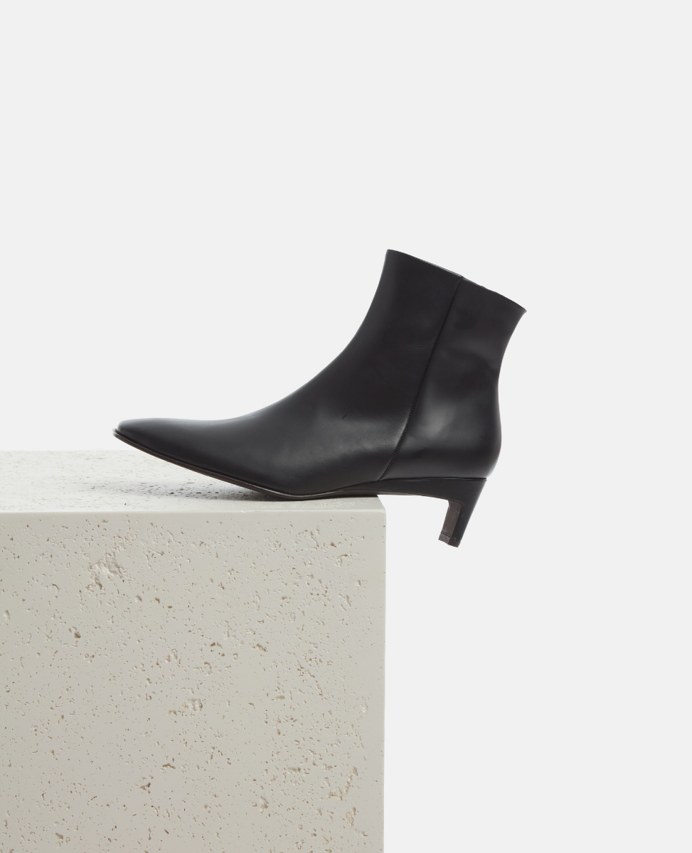 Black ankle boot on a light gray surface with a white background