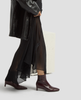 Person wearing a black coat, sheer black skirt, and brown ankle boots on a light gray background 5