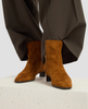 Brown suede boots worn with a dark coat on a light background 6