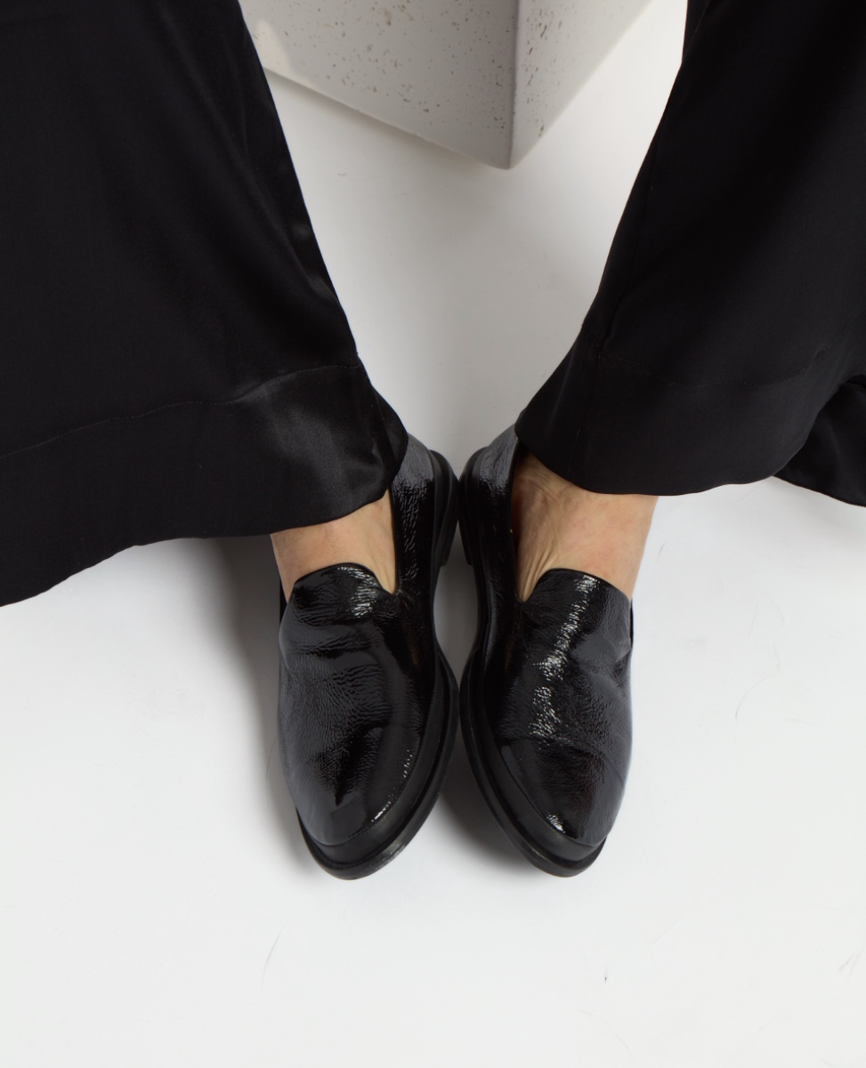 Shiny black leather loafers with a sleek, smooth texture and a low heel, featuring a minimalist design and rounded toe.