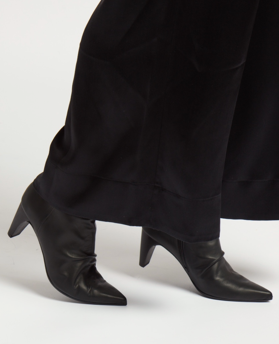 Sleek black leather ankle boots with pointed toes, a smooth texture, and mid-height stiletto heels, partially covered by long black pants.