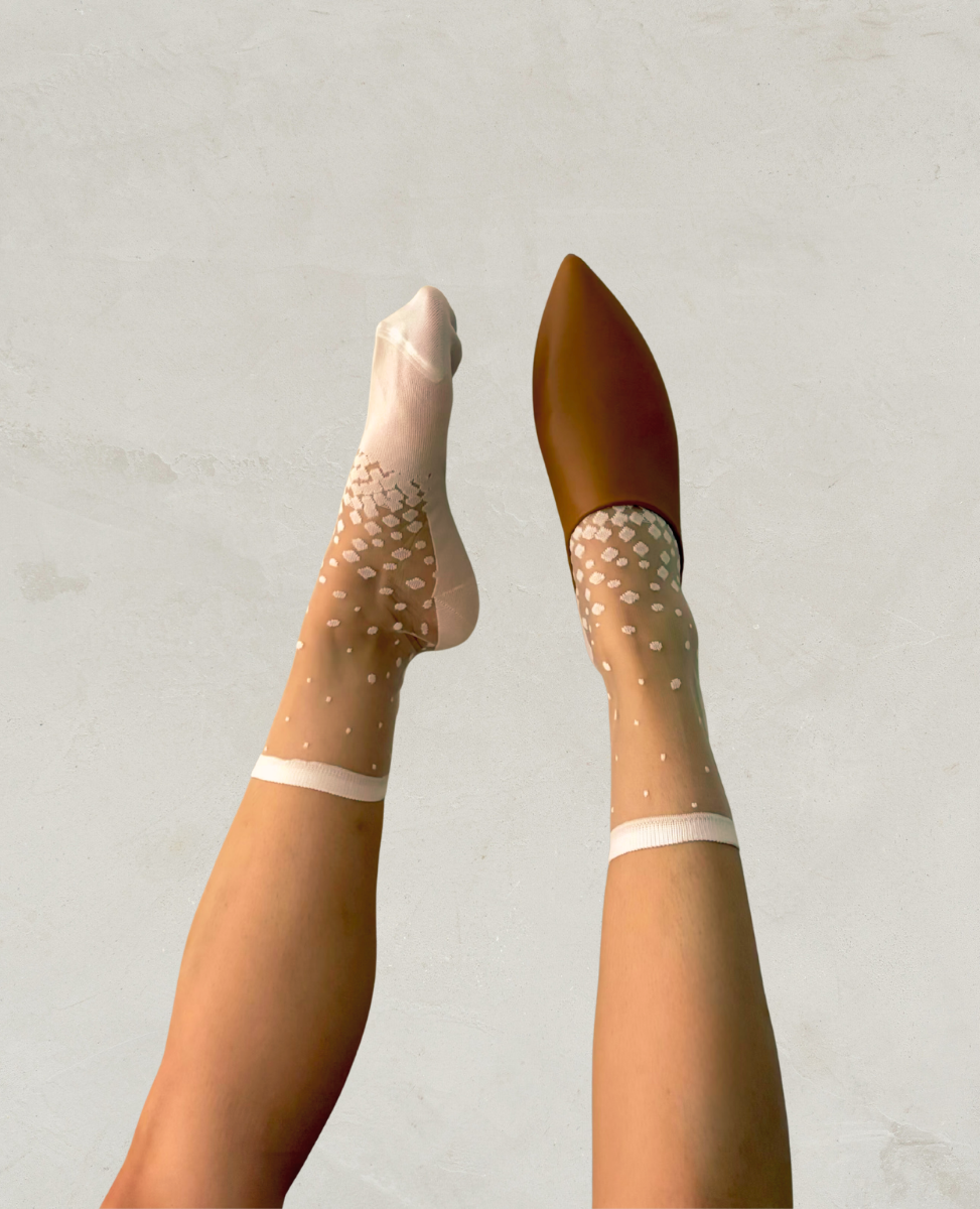 Sheer stockings with white polka dots worn by a person on a light gray background