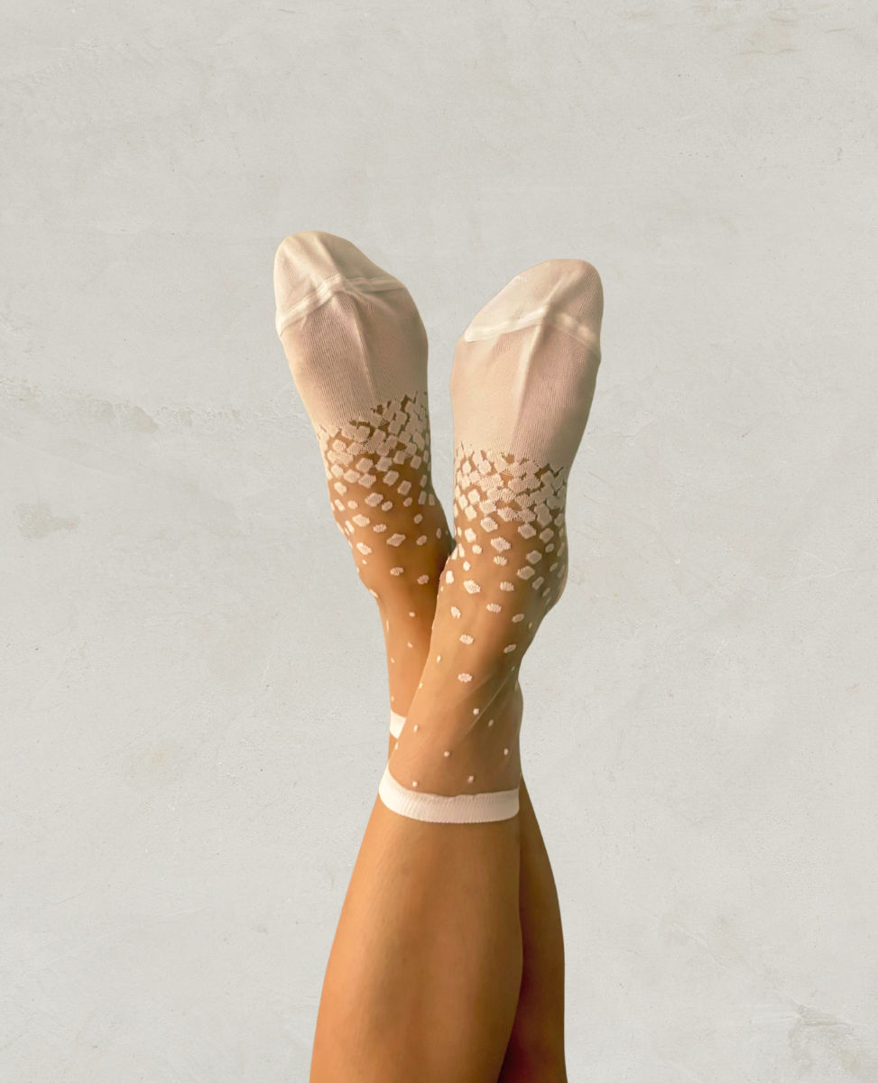 Sheer beige socks with white floral pattern worn by a person on a light gray background