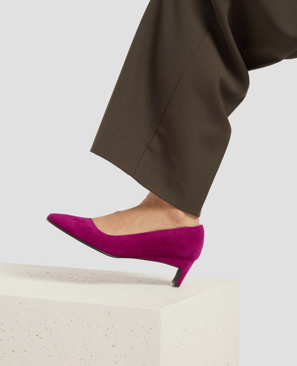 Purple high-heeled shoes worn with brown pants on a light background