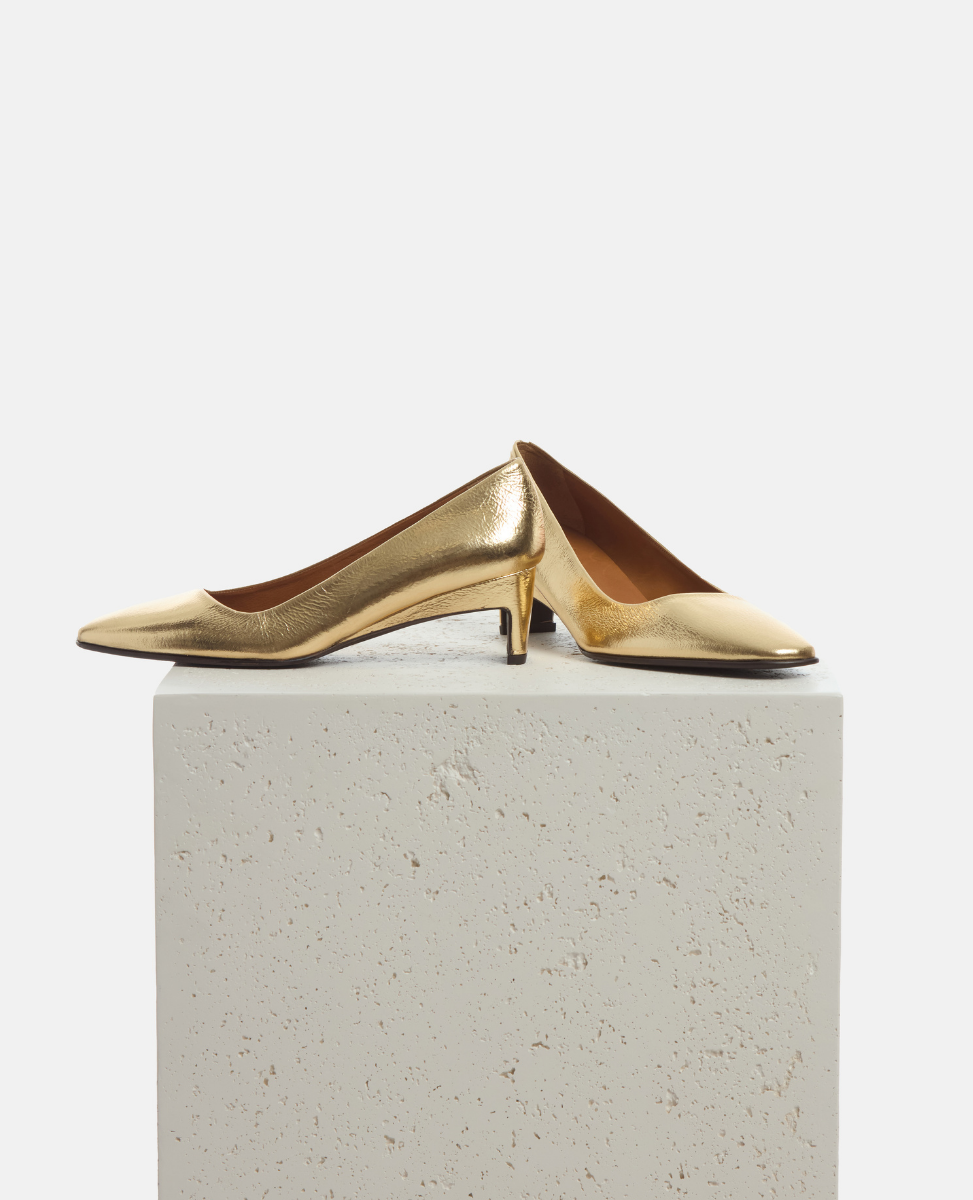 Gold high-heeled shoes on a light gray pedestal against a white background