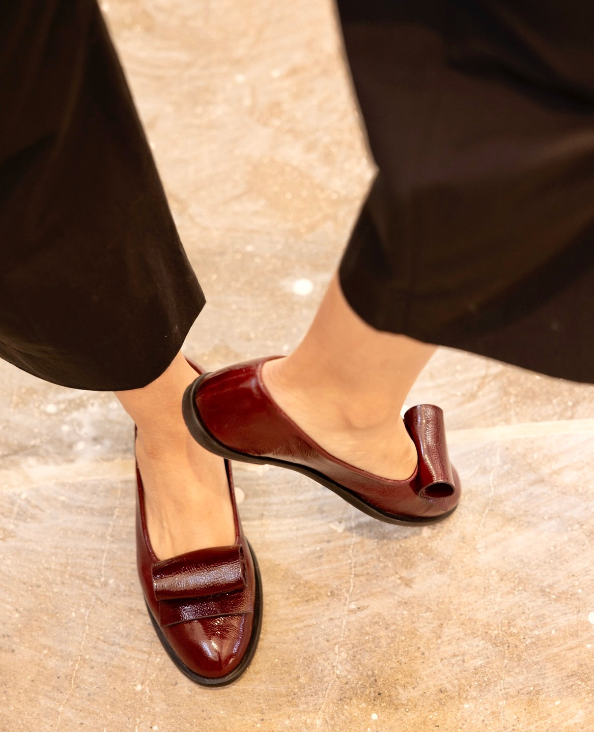 A person wearing black pants and burgundy loafers stands on a light-colored floor.