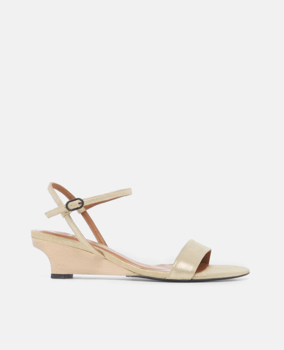 A sleek, gold sandal with a low wedge heel, featuring a thin ankle strap with a small buckle and a single wide toe strap, crafted from a suede.