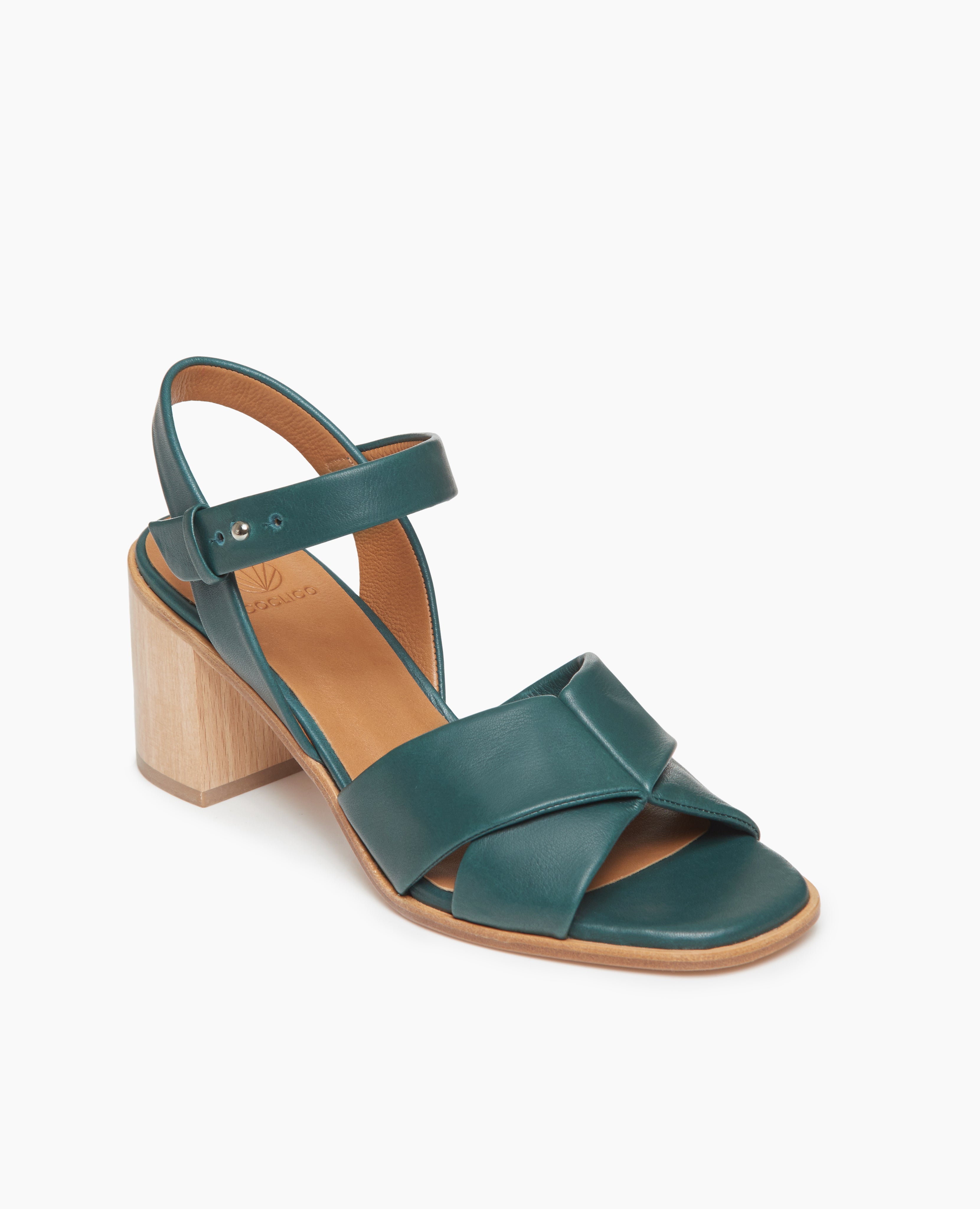 Coclico Bay Heel in Riviera leather, angled view: open sandal with 2 tubular straps across the foot, ankle strap, peg closure, wood block mid-height heel.