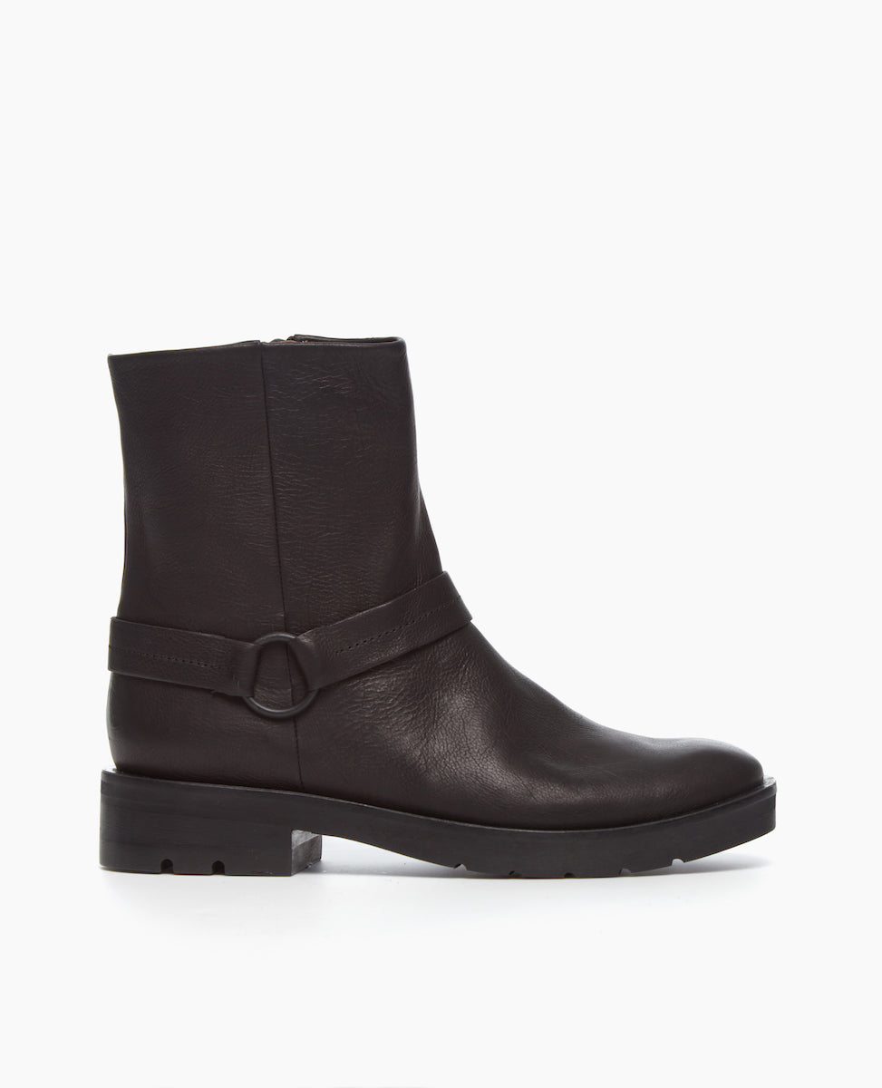 Side view of the Damiana Shearling Boot: a full shearling lined modern moto boot, featuring a belt and loop at the ankle, a lug sole, and an inside-zip closure.