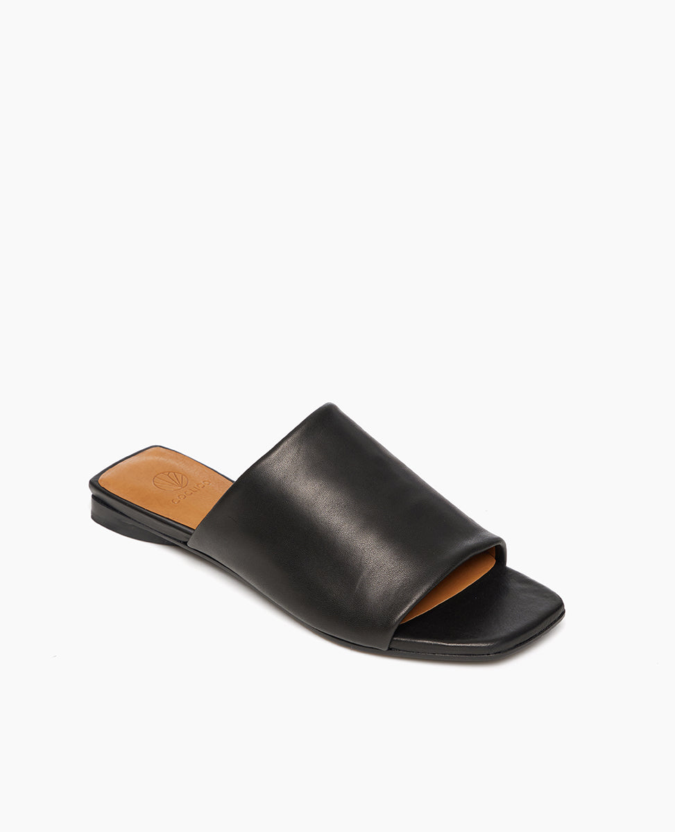 Coclico Ferhana Sandal in Black leather, angled view: flat slide-on style with one solid band of leather, squared-off at the toe and heel.