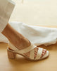 Model seated wearing the Coclico Jade Heel in Greige leather: a wood block mid-height heel with leather tube straps across arch, sling-back strap. 5