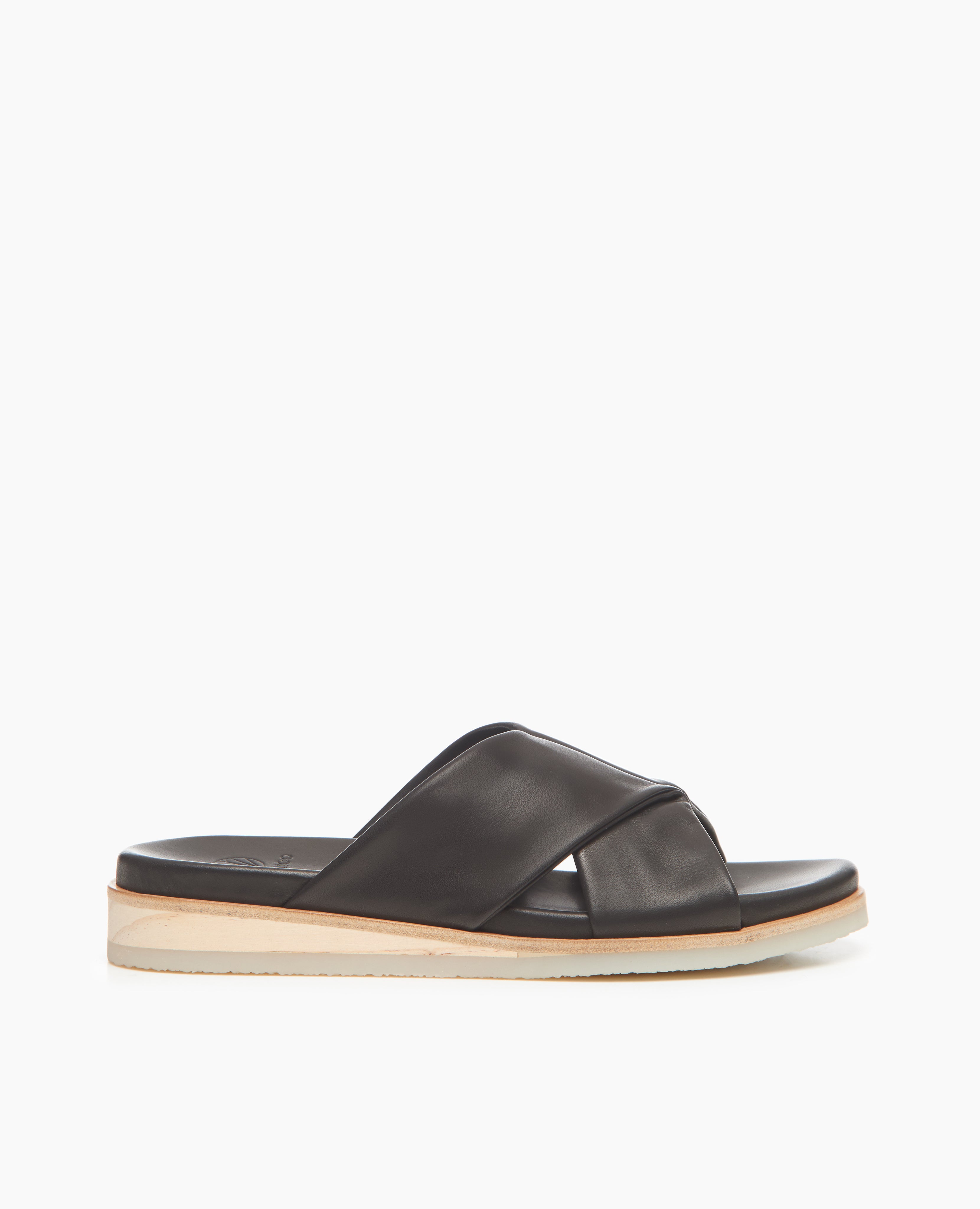 Side view of Coclico Pasque Sandal in Black leather, a low pine wedge slide sandal with rubber sole and intertwined leather tube straps across foot.