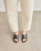 Top view of model in Coclico Pasque Sandal in Black leather: a low pine wedge slide sandal, rubber sole, intertwined leather tube straps across foot. 3