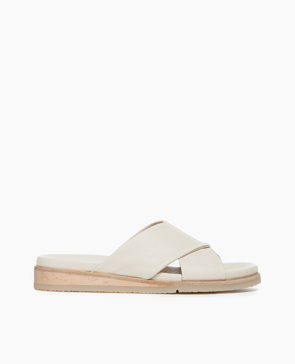 Side view of Coclico Pasque Sandal in Greige (off-white) leather, a low pine wedge slide sandal with rubber sole and intertwined leather tube straps across foot.