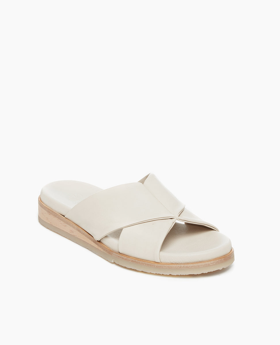 Coclico Pasque Sandal in Greige (off-white) leather, a low pine wedge slide sandal with rubber sole and intertwined leather tube straps across foot - angle view.