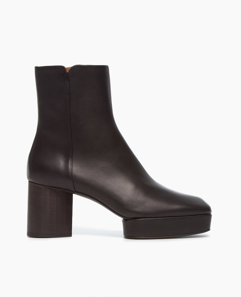A sleek, black leather ankle boot with a smooth texture, featuring a squared toe, a side zipper, and a chunky, block heel.
