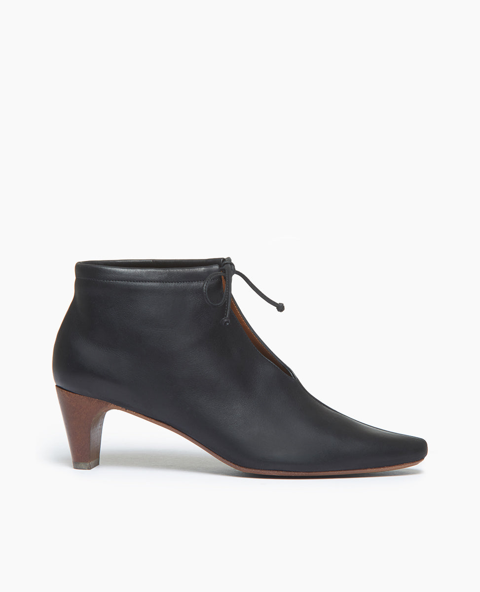 Side view of the Waffles Bootie in Black Leather; featuring a softly arched solid wood heel and gathered tie at the ankle revealing just enough to be both feminine and practical.