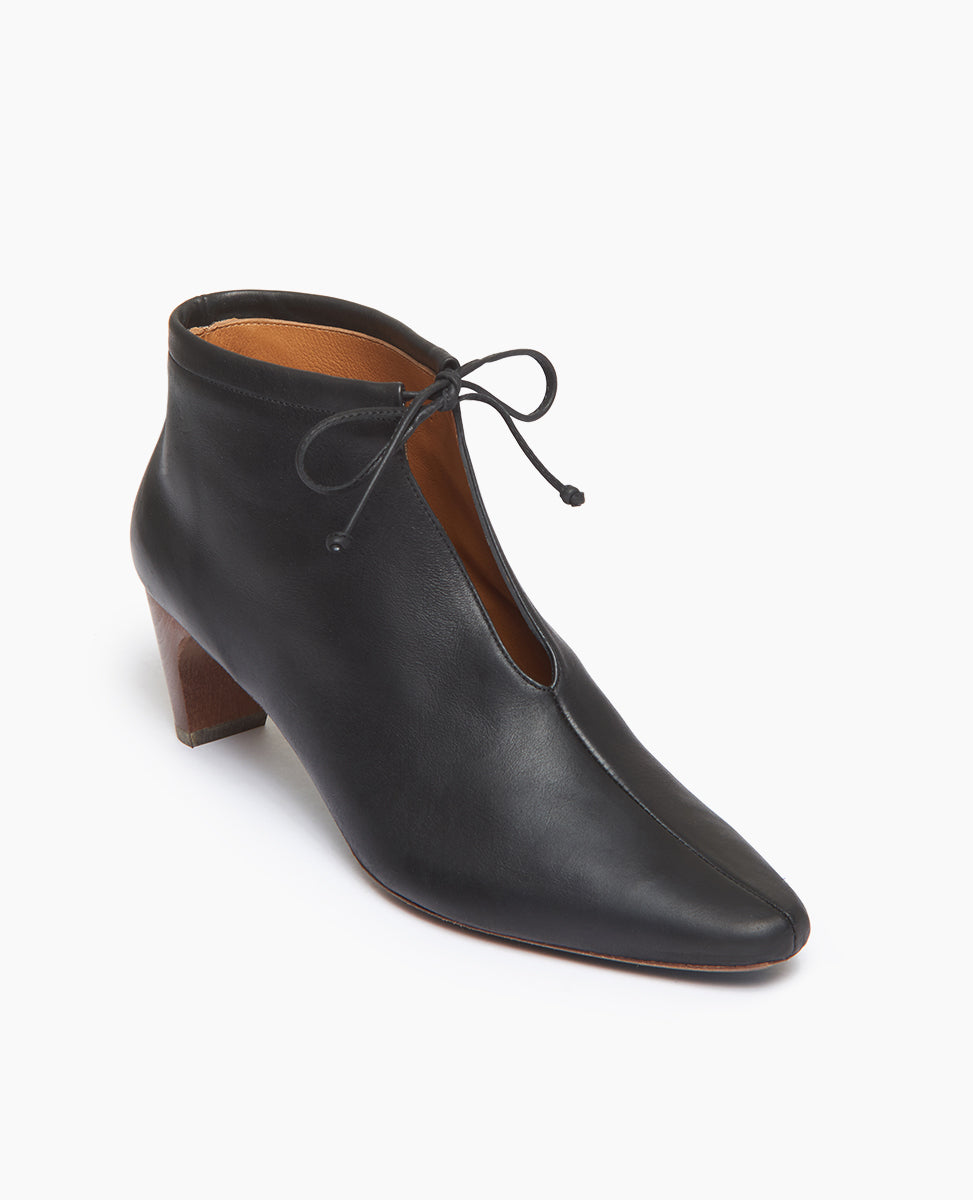 Coclico Waffles Bootie in Black Leather; angled view featuring a softly arched solid wood heel and gathered tie at the ankle revealing just enough to be both feminine and practical.