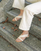 Close up of model sitting on stairs wearing Coclico Cardinal Sandals in greige leather. 2