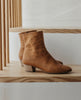 Side view of Coclico Caviar Boot in Mandorla leather, a simple & modern boot with a low-height wood block heel, tall shaft height and inside zip closure - on wooden steps. 5