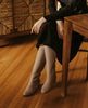 Top view of woman seated cross legged on a chair modeling the Coclico Chip Boot in Limestone nubuck. 6