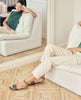 Model sitting wearing the Coclico Erren Sandal in Deep Sea leather: open sandal with leather front band, raised two-part wood and leather sole, tubular ankle strap that crisscrosses behind the heel. 3