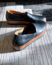 The Gentian Flat in Black leather: a slip-on flat with leather band and .5 inch rubber EVA sole displayed in sunlight on carpet.  8