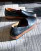 The Gentian Flat in Black leather: a slip-on flat with leather band and .5 inch rubber EVA sole displayed in sunlight on carpet. 8