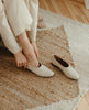Woman putting on the Coclico Haloumi Flat in Greige leather - top view. 4