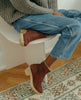 Close up of model in the Coclico Keep Shearling Clog in Britannic leather, a shearling-lined clog with tapered, inside zip closure, snipped toe, mid-height wood block platform - on stool. 3