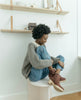 Woman sitting cross-legged on stool modeling the Coclico Keep Shearling Clog in Britannic leather, a shearling-lined clog with tapered, snipped toe, mid-height wood block platform. 2