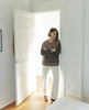 Woman leaning on door frame wearing a shearling-lined clog with tapered, snipped toe, inside zip closure, mid-height wood block platform. 8