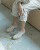 Model sitting on Coclico Kera Shearling Clog in Latte nubuck. 3
