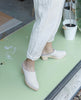 Woman wearing a slip-on mule with a mid-height wood block base, tapered toe, shearling lining - in an art studio. 5