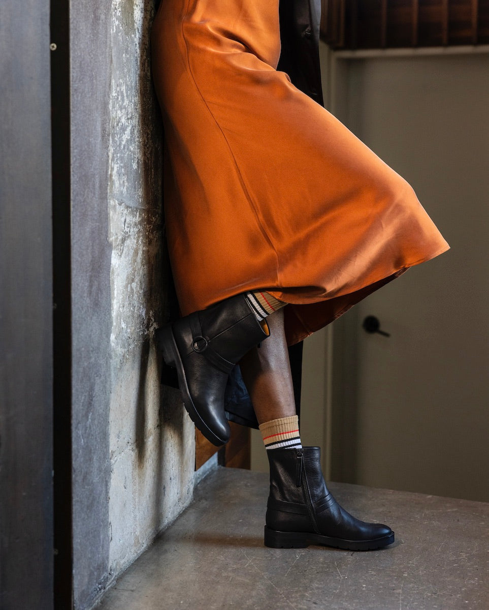 Legs of woman leaned up against a cement wall wearing the Damiana Shearling Boot with the right leg propped up on the wall.