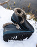 The Fiona Shearling Bootie in Deep Sea lying in nature on top of snow with the right shoe laying on its side.  4