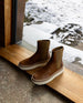 Pair of the France Boot in Caramello in the middle of a wooden doorway with a snowy landscape behind.  2