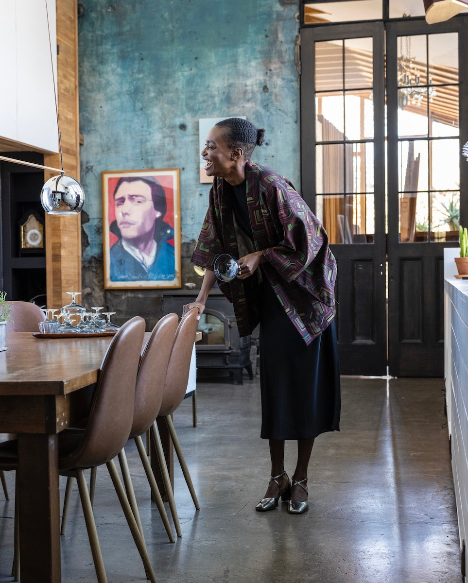 Woman standing, resting her hand on a chair while laughing and wearing the Isabel Mary Jane in Starry Night with a top draped over a long blue dress.