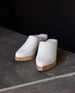 Front view of the Kera Shearling Clog in Griege Nubuck against a black background and a cement table. 4