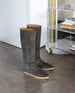 Coclico Quest Boot in Anthracite placed on a concrete floor with acrylic shelves in the back.  3